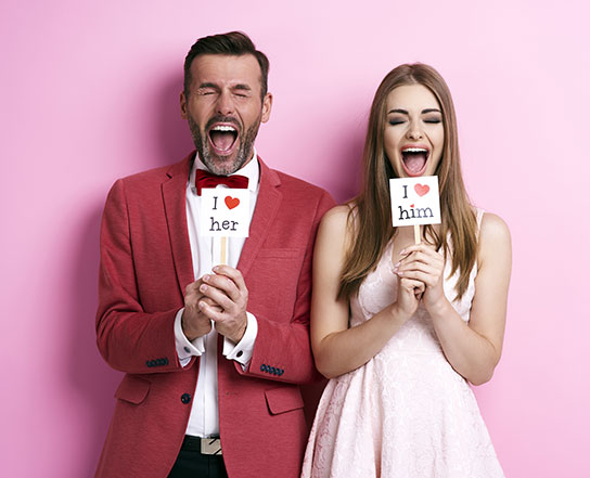 Couple laughing holding signs that say, "I love her" and "I love him"